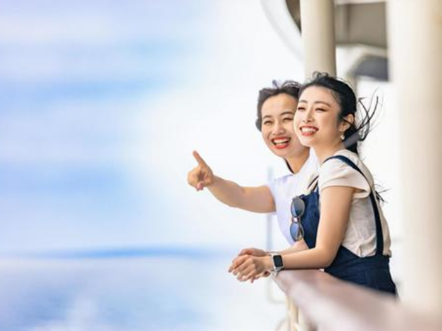 船のデッキから海を眺め、笑顔で遠くを指差す二人の女性。