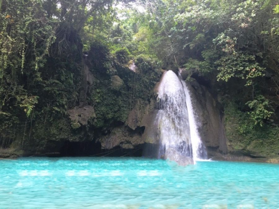 フィリピン・セブ島のカワサン滝。豊かな緑に囲まれた岩山から、鮮やかなエメラルドグリーンの滝つぼへ流れ落ちる滝の全景。