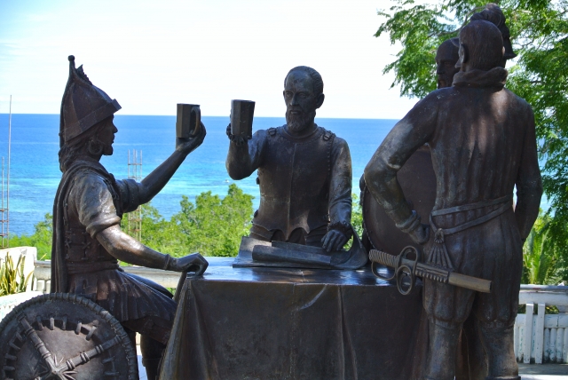 A bronze statue of the Blood Compact Monument on Bohol Island, set against the backdrop of the ocean