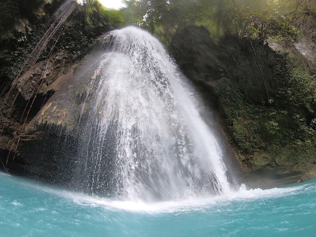 A beautiful emerald-green pool and a majestic waterfall, surrounded by the lush natural beauty of Bohol Island